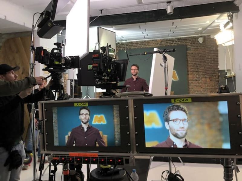 Scene of a video production, two screens show Dominik Schwarz who is also visible in the background.
