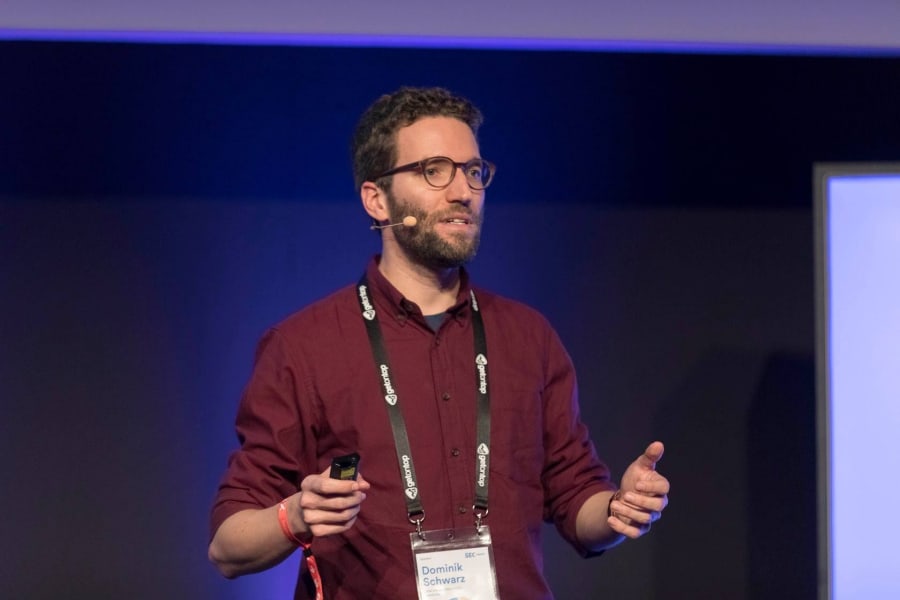 Dominik Schwarz is wearing a red shirt, a lanyard and a presenters microphone.