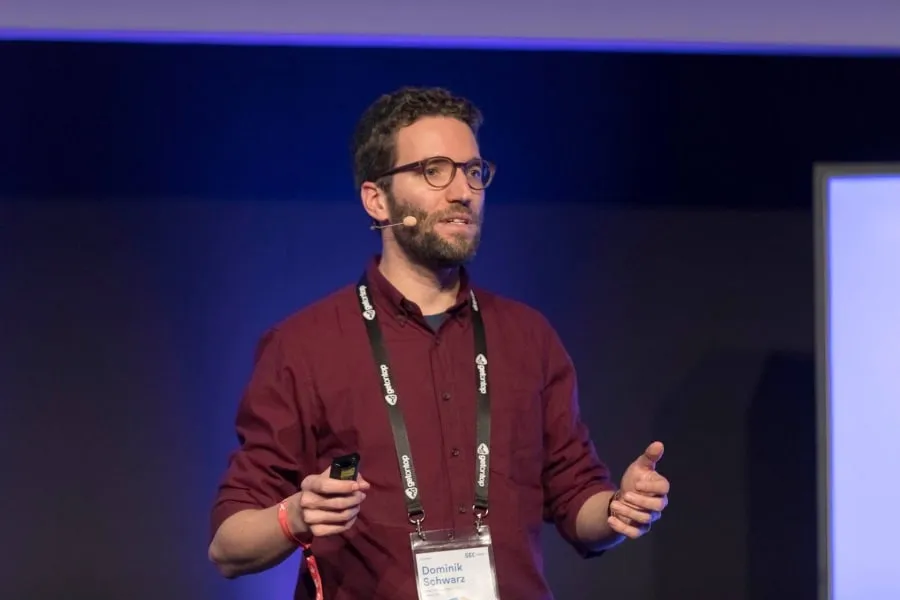 Dominik Schwarz is wearing a red shirt, a lanyard and a presenters microphone.